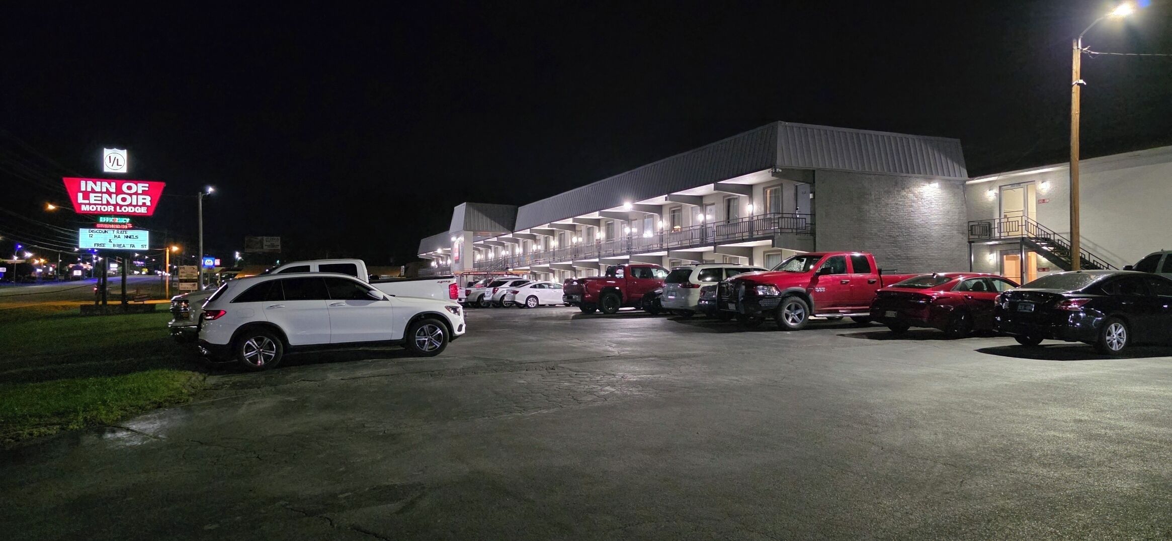 A parking lot with multiple vehicles, a building with a modern design, and a sign for the Inn of Lenoir Motor Lodge.