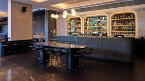A modern bar area with a central island and multiple stools, surrounded by shelves stocked with bottles and glasses. - Pullman Adelaide (Adelaide)