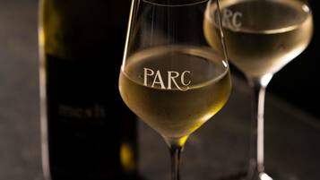 Deux verres de vin blanc, dont l’étiquette porte l’inscription « PARC », posés sur une surface sombre.