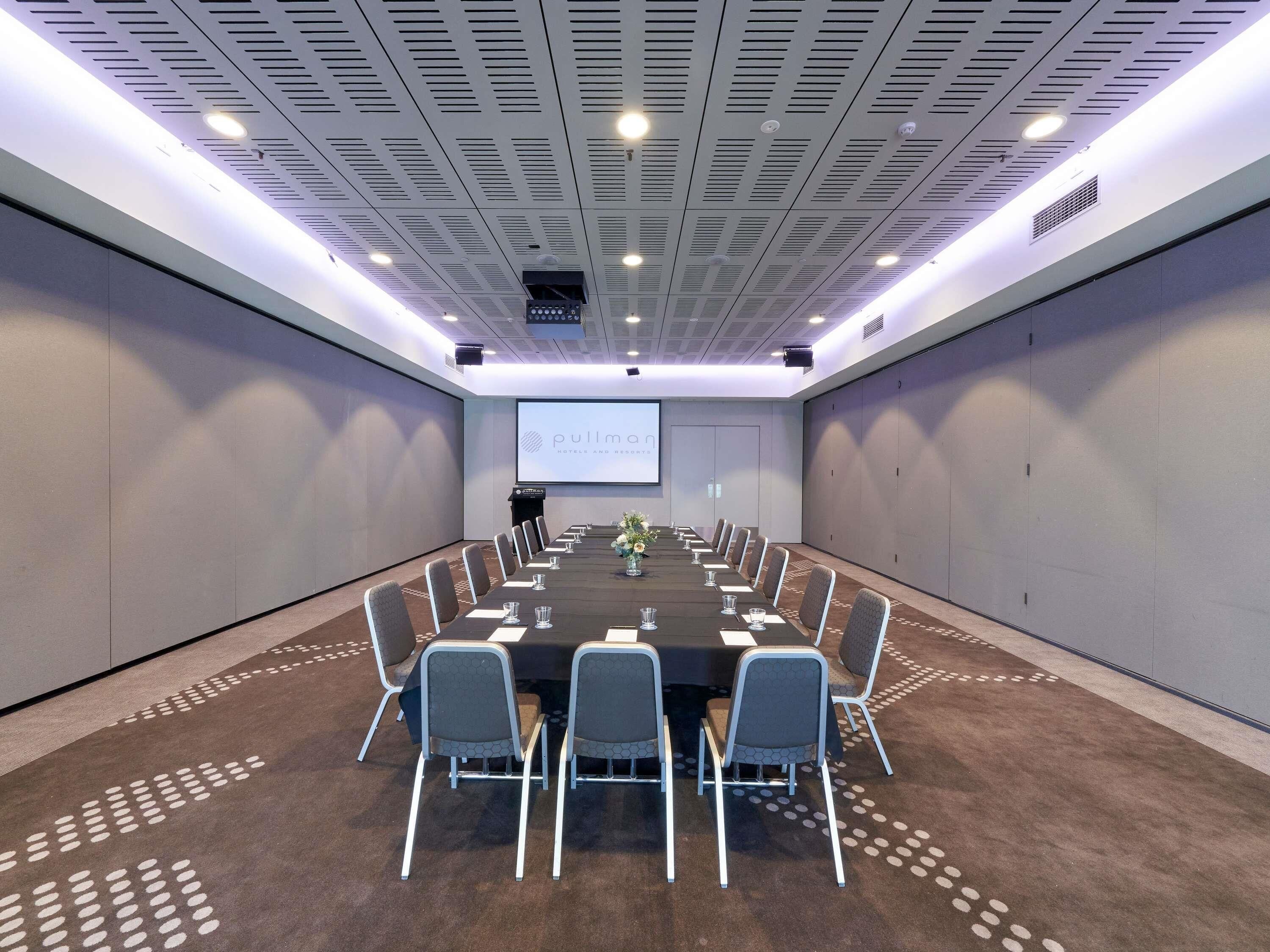 A conference room with a long table, chairs, a projector screen, and a carpeted floor.