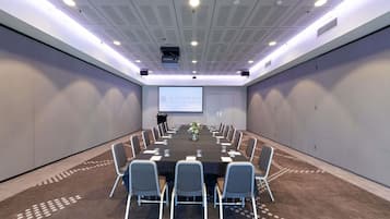 A conference room with a long table, chairs, a projector screen, and a carpeted floor.