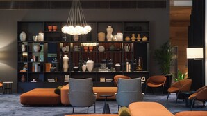 A modern living room with orange sofas, a black and white checkered chair, and a large bookshelf filled with decorative items. - Pullman Adelaide (Adelaide)