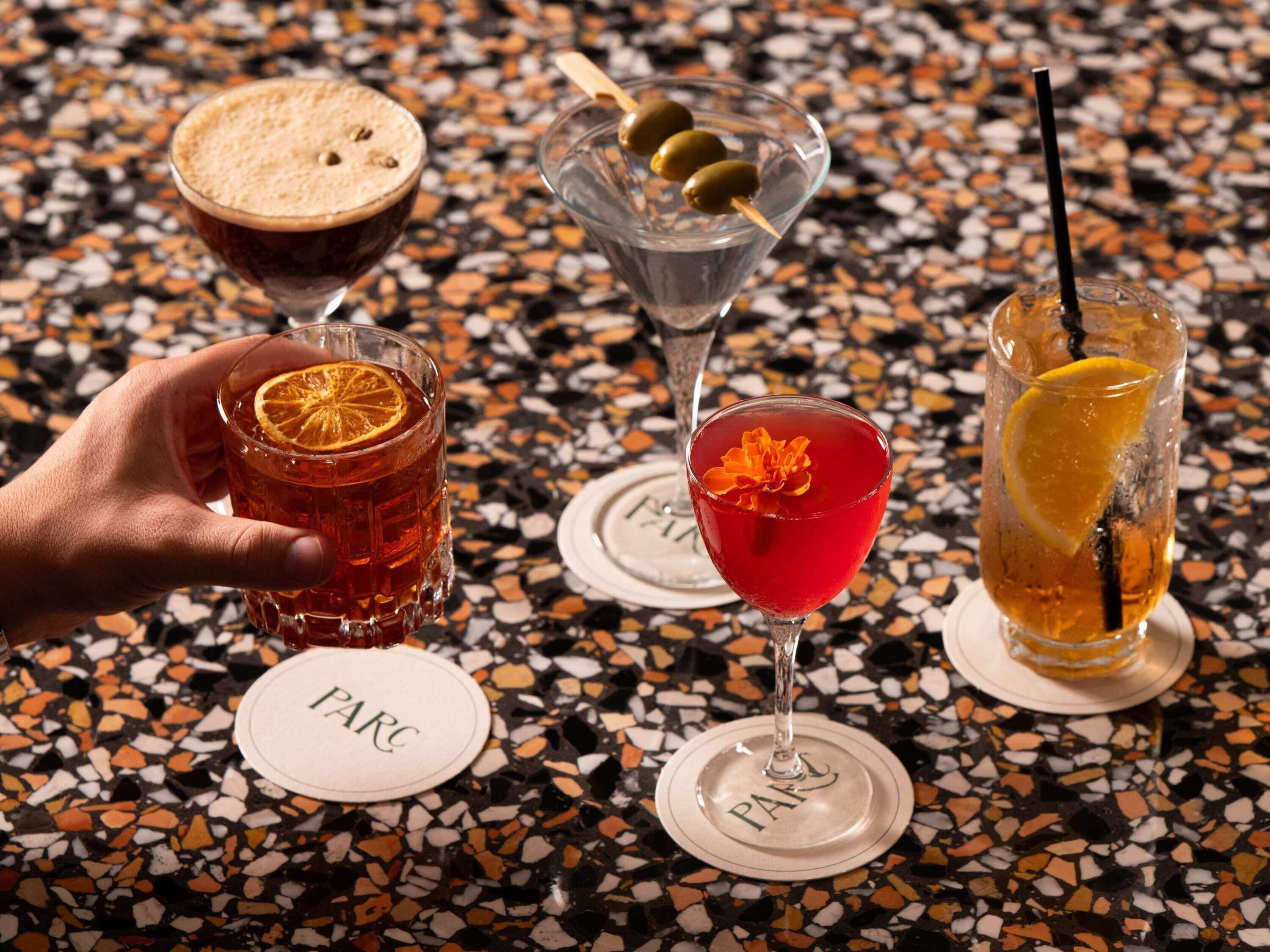 Three cocktails on a terrazzo table with a hand holding one.