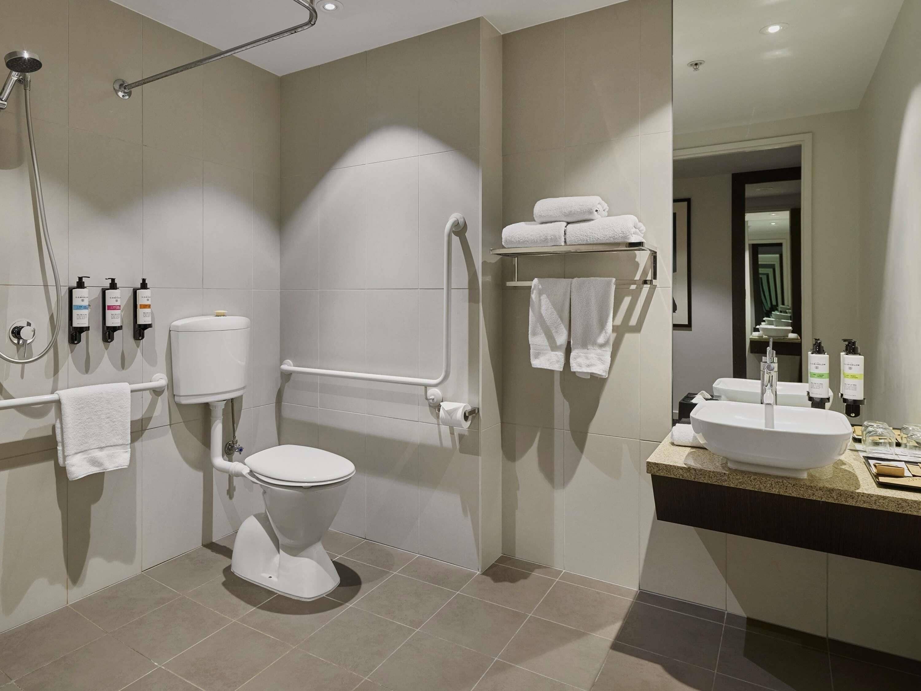 A modern bathroom with a toilet, bidet, hand dryer, and a sink with a mirror.