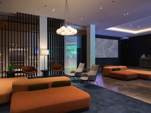 A modern lobby with orange seating, a unique ceiling light, and a digital wall display. - Pullman Adelaide (Adelaide)