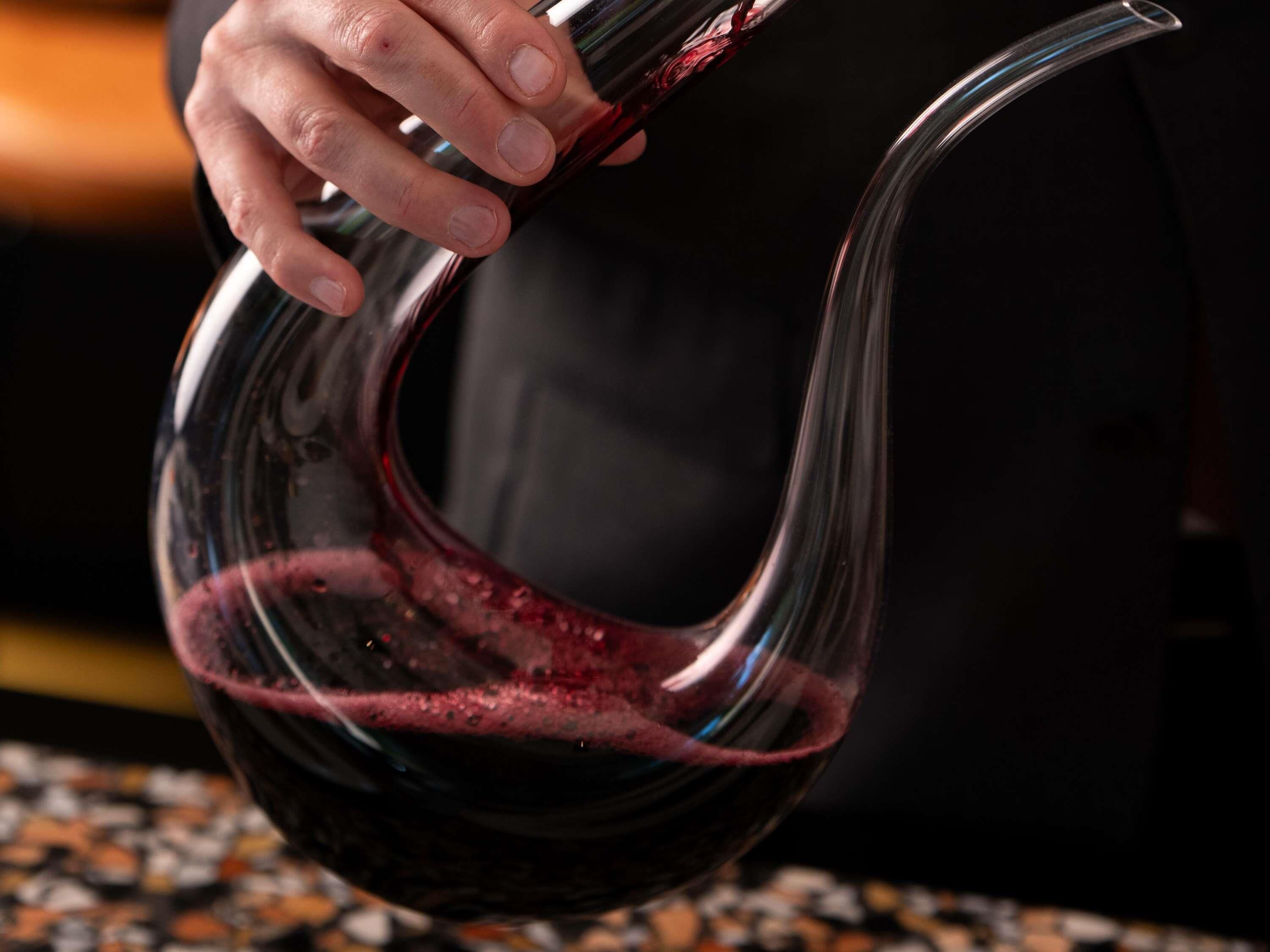 Una mano che tiene un bicchiere da vino pieno di vino rosso.