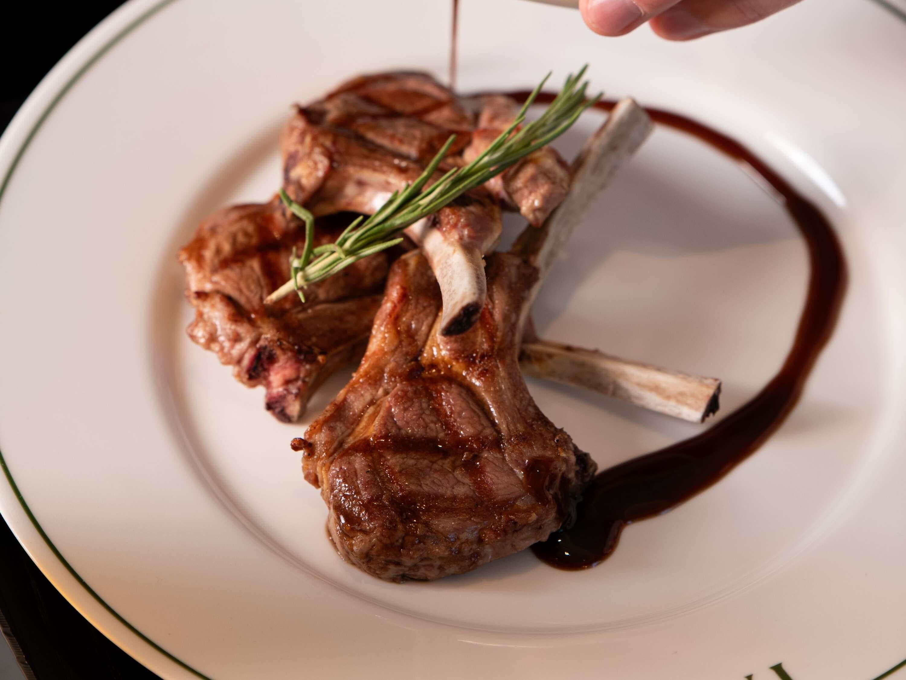 A plate with a lamb chop, rosemary, and a dark sauce.