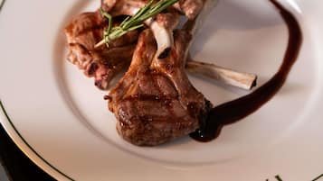 A plate with a lamb chop, rosemary, and a dark sauce.