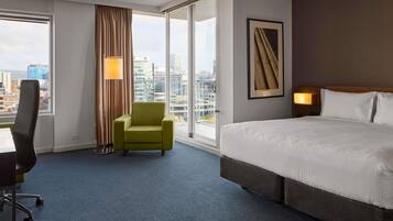 Una habitación de hotel con una cama grande, una silla, un escritorio y un ventanal con vistas a la ciudad.