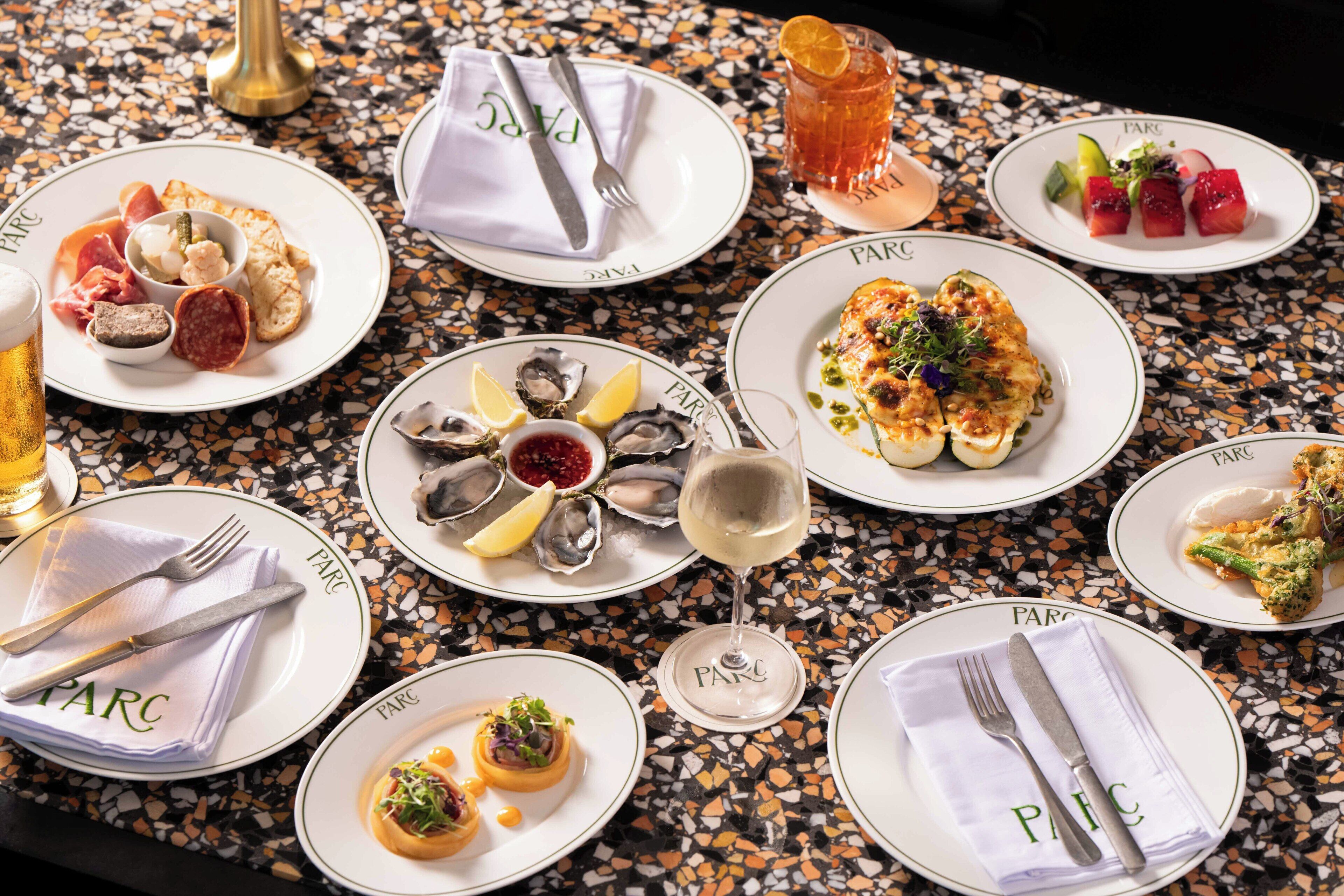 A table set with various dishes, including seafood, salads, and appetizers, on a speckled tile table.