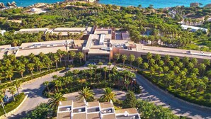 An aerial view of a resort with a central building surrounded by palm trees and a coastline. - Kimpton Atlântico Algarve by IHG (Albufeira)