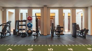 A gym with exercise equipment, a green turf floor with numbers, and large windows.