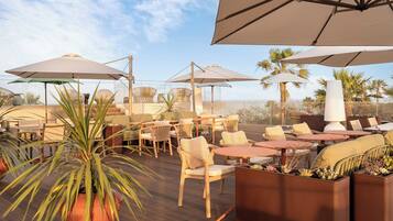 An outdoor seating area with tables and chairs, umbrellas, and potted plants.
