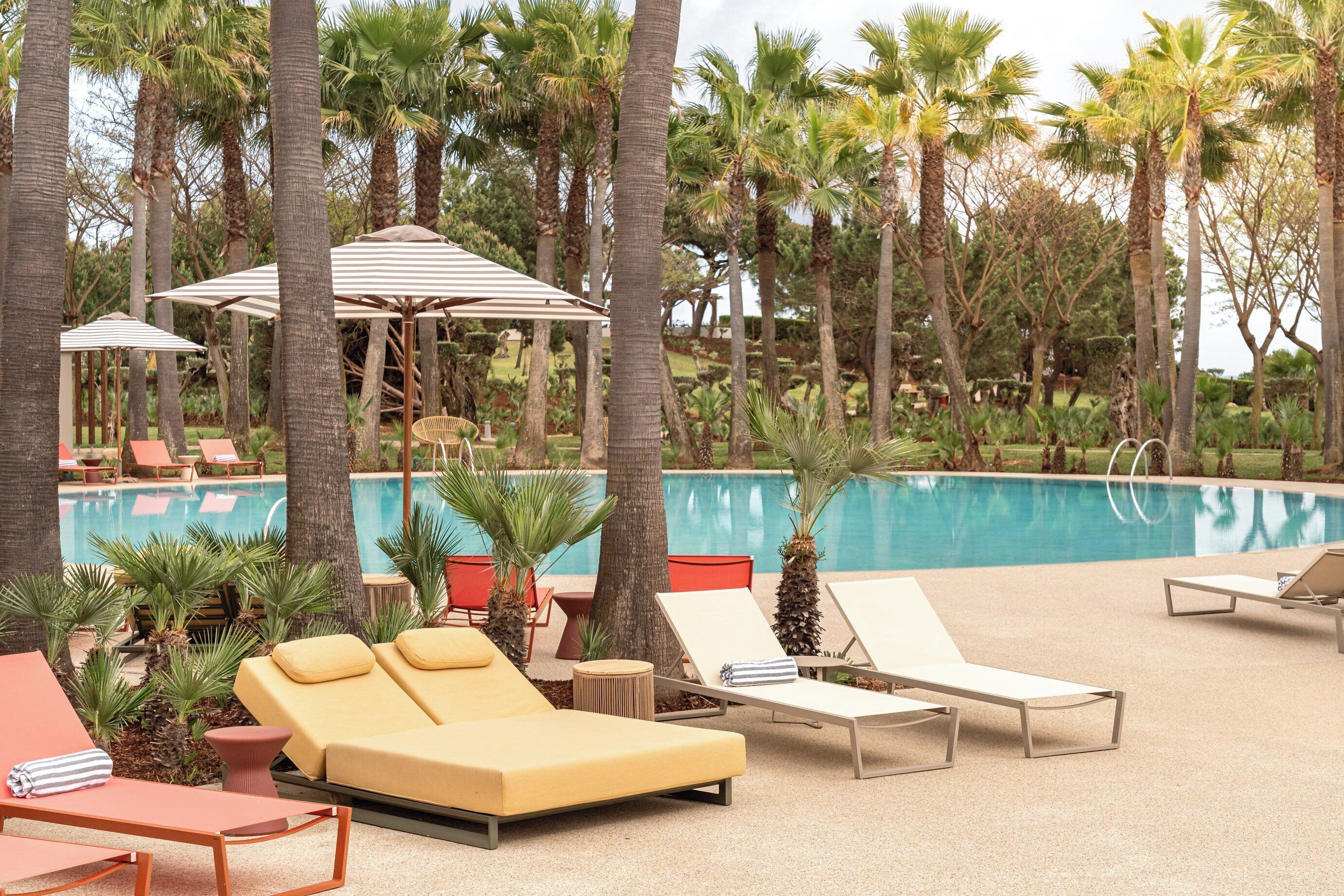 A poolside area with lounge chairs, umbrellas, and palm trees.