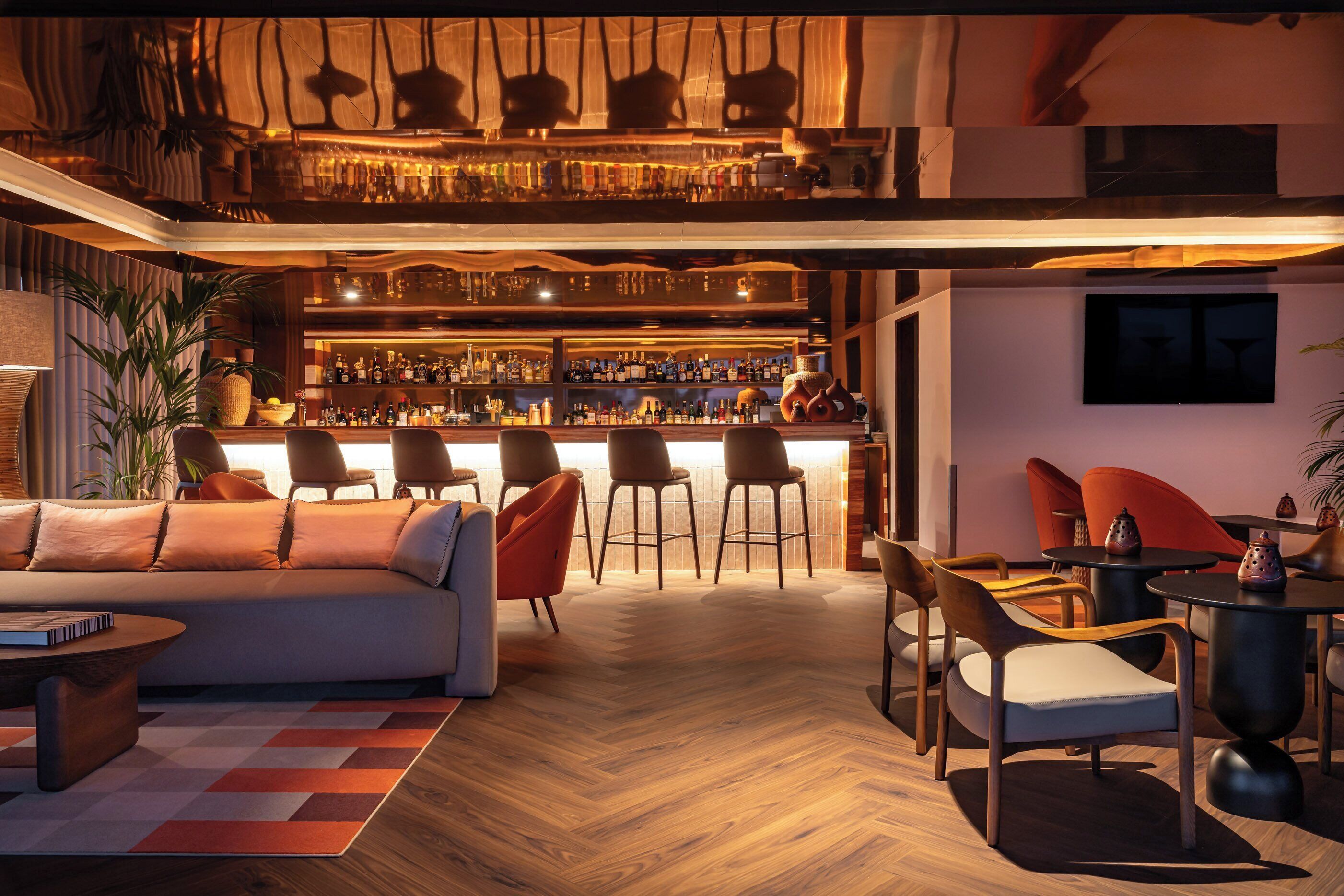 Uma área de bar moderna com teto alto, vigas de madeira e diversas opções de assento, incluindo banquetas e cadeiras.