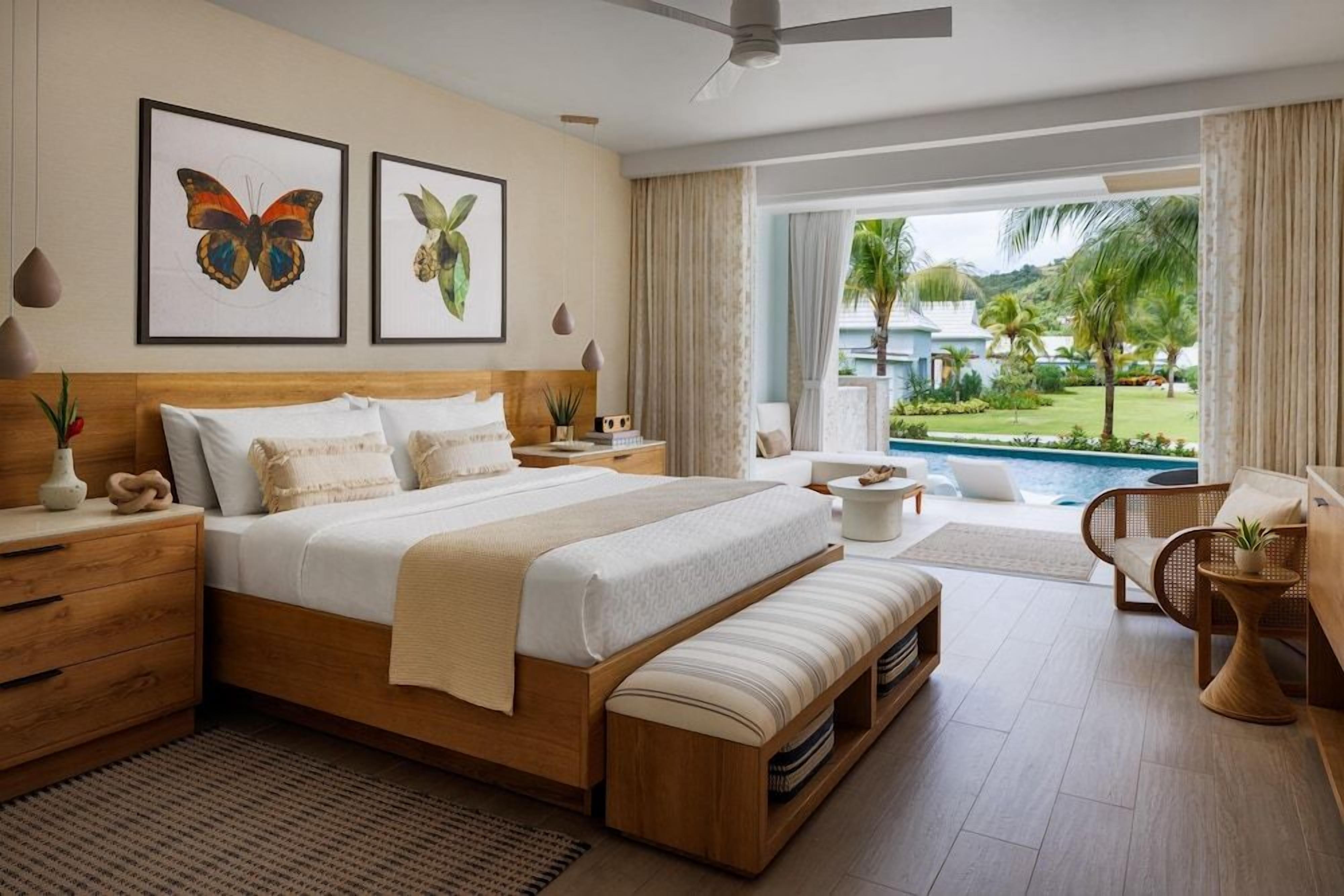 A modern bedroom with a large bed, bedside tables, a bench, and a view of a pool and greenery.
