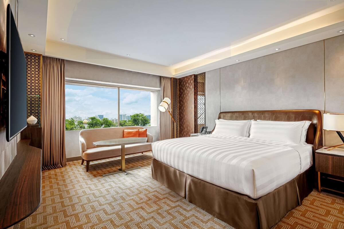 Quarto de hotel moderno com uma cama grande, um sofá, uma TV e vista para a cidade.
