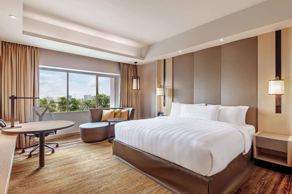 Quarto de hotel com uma cama grande, uma escrivaninha, um sofá e vista para a cidade.