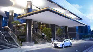 A modern hotel entrance with a covered walkway, a staircase, and a car parked outside.