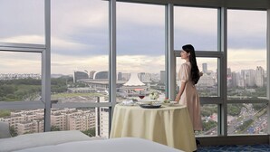 A hotel room with a large window offering a city view, a neatly arranged dining table with a wine glass, and a person standing by the window. - Nanning Marriott Hotel (Nanning)