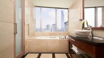 A modern bathroom with a large bathtub, a sink, and a vanity. It features a city view through large windows.
