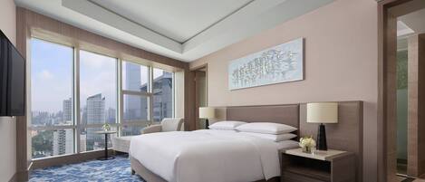 Una habitación de hotel moderna con una cama grande, una mesita de noche, un televisor y vistas a la ciudad a través de amplios ventanales.