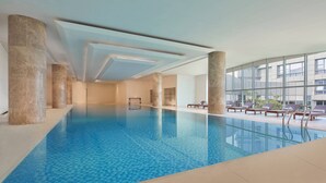 An indoor swimming pool with clear blue water, surrounded by marble columns and large windows offering views of the outside. - Nanning Marriott Hotel (Nanning)