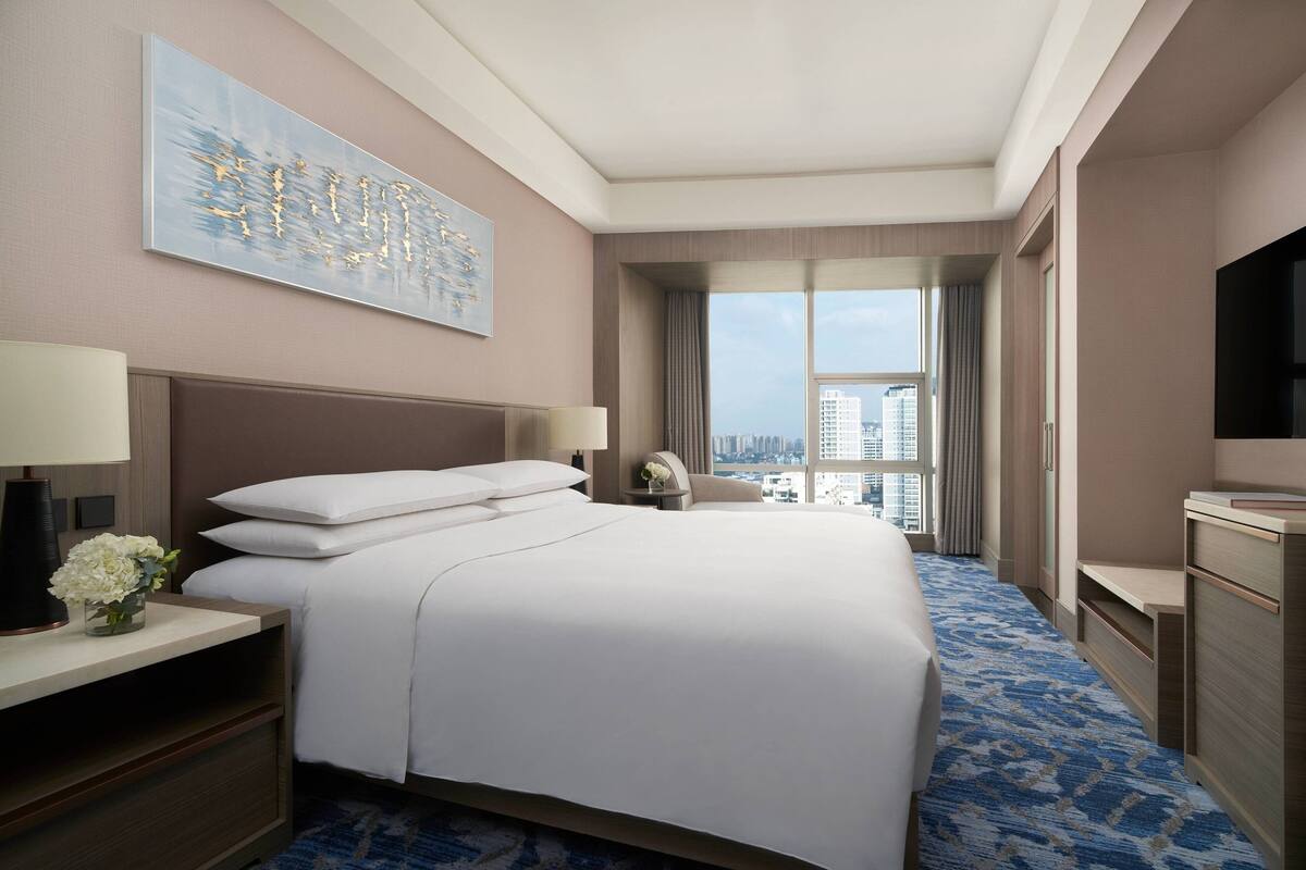 Habitación de hotel con una cama grande, televisión, escritorio con lámpara y vistas a la ciudad.