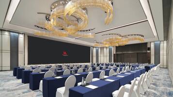 A conference room with rows of tables, white chairs, and a large screen.