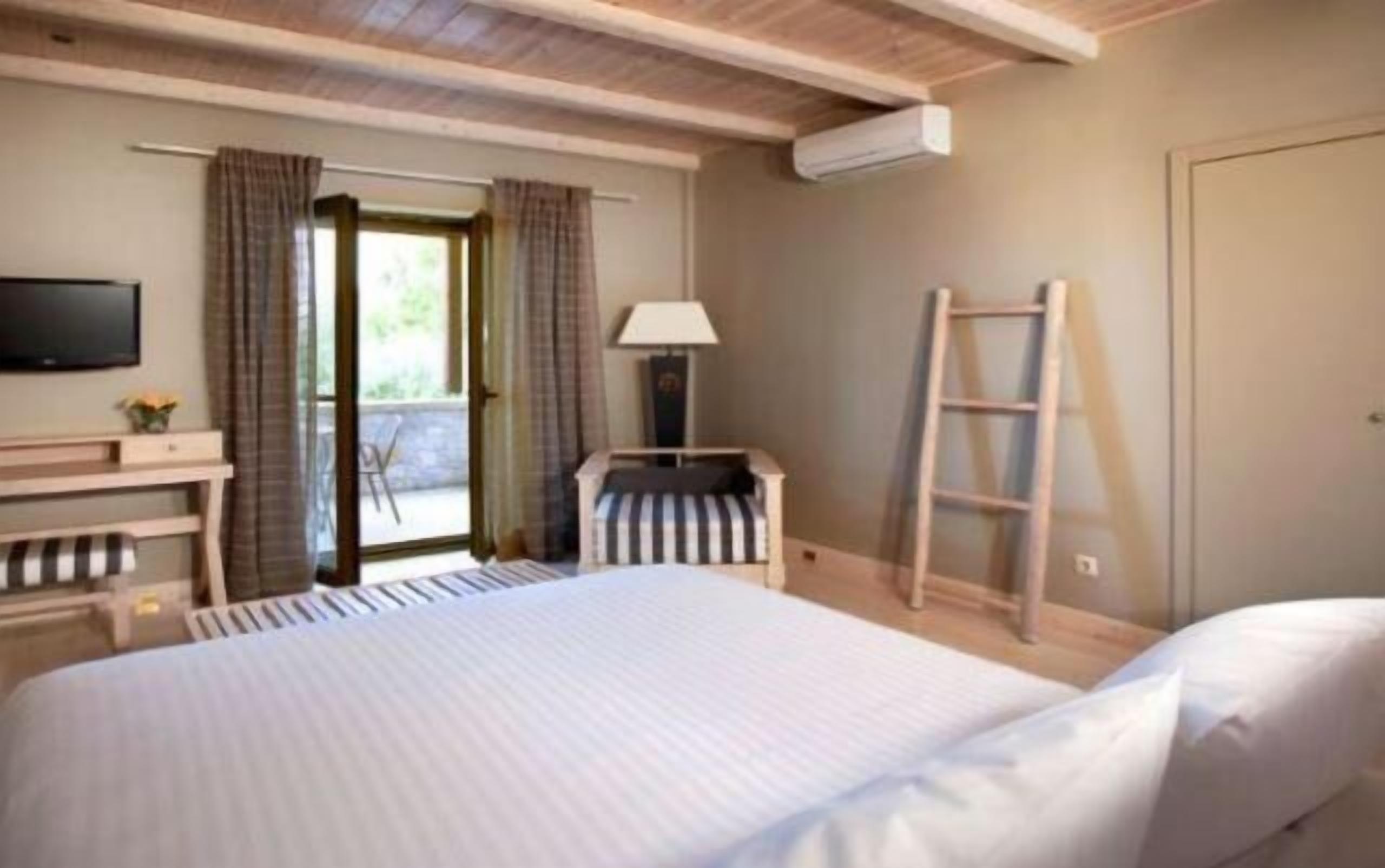 A hotel room with a bed, a desk, a chair, a TV, a lamp, and a ladder.