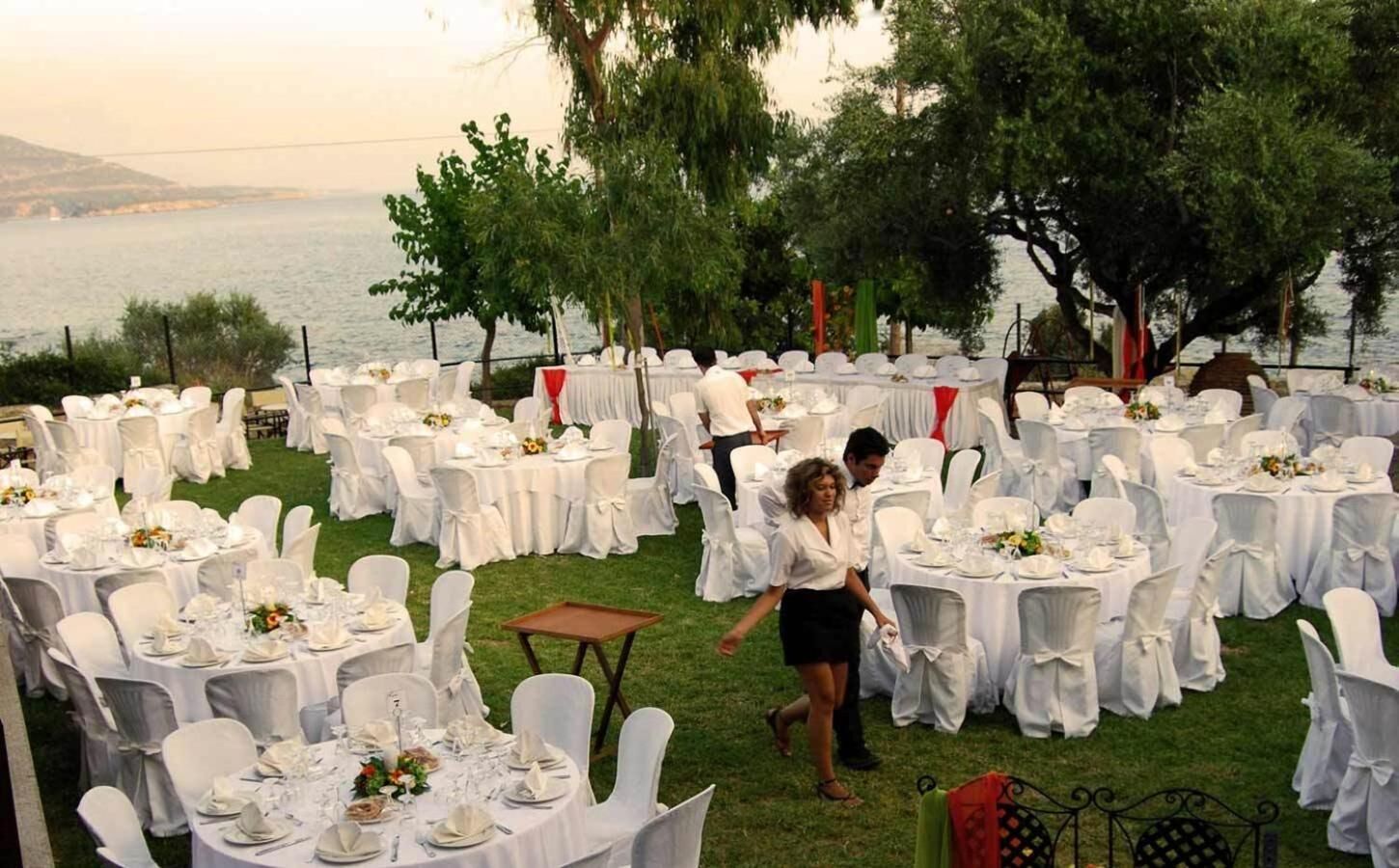 An outdoor wedding reception with round tables set up on grass, overlooking a body of water.