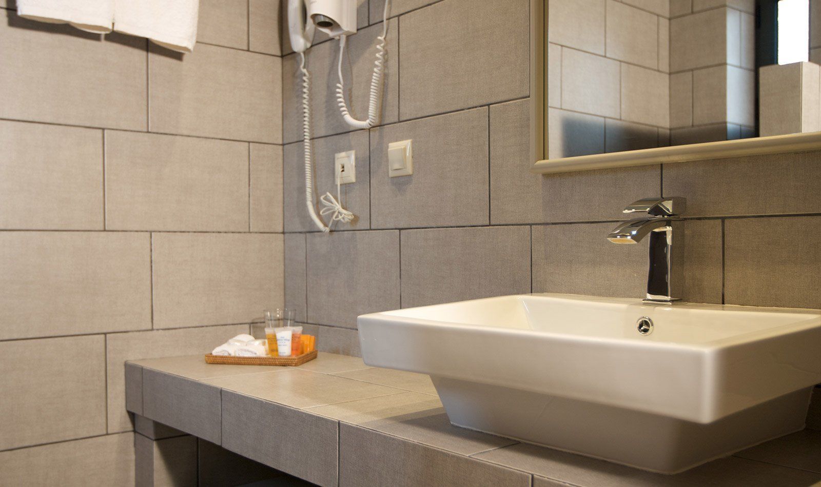 Un baño con un lavamanos grande, un espejo y un secador de pelo en la pared.