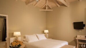 Ein Schlafzimmer mit Holzboden, einem Bett mit weißer Bettwäsche, zwei Nachttischlampen, einem kleinen Tisch mit Blumenvase und einem Fernseher an der Wand.