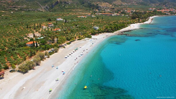 Eine Küstenstadt mit Strand, Häusern und Bergen im Hintergrund.