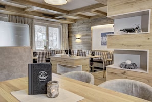 A modern kitchen with wooden cabinetry, a dining area with a wooden table and chairs, and a built-in shelf with decorative items. - Hotel-Restaurant Bike&Snow Lederer (Muehlbach Am Hochkoenig)