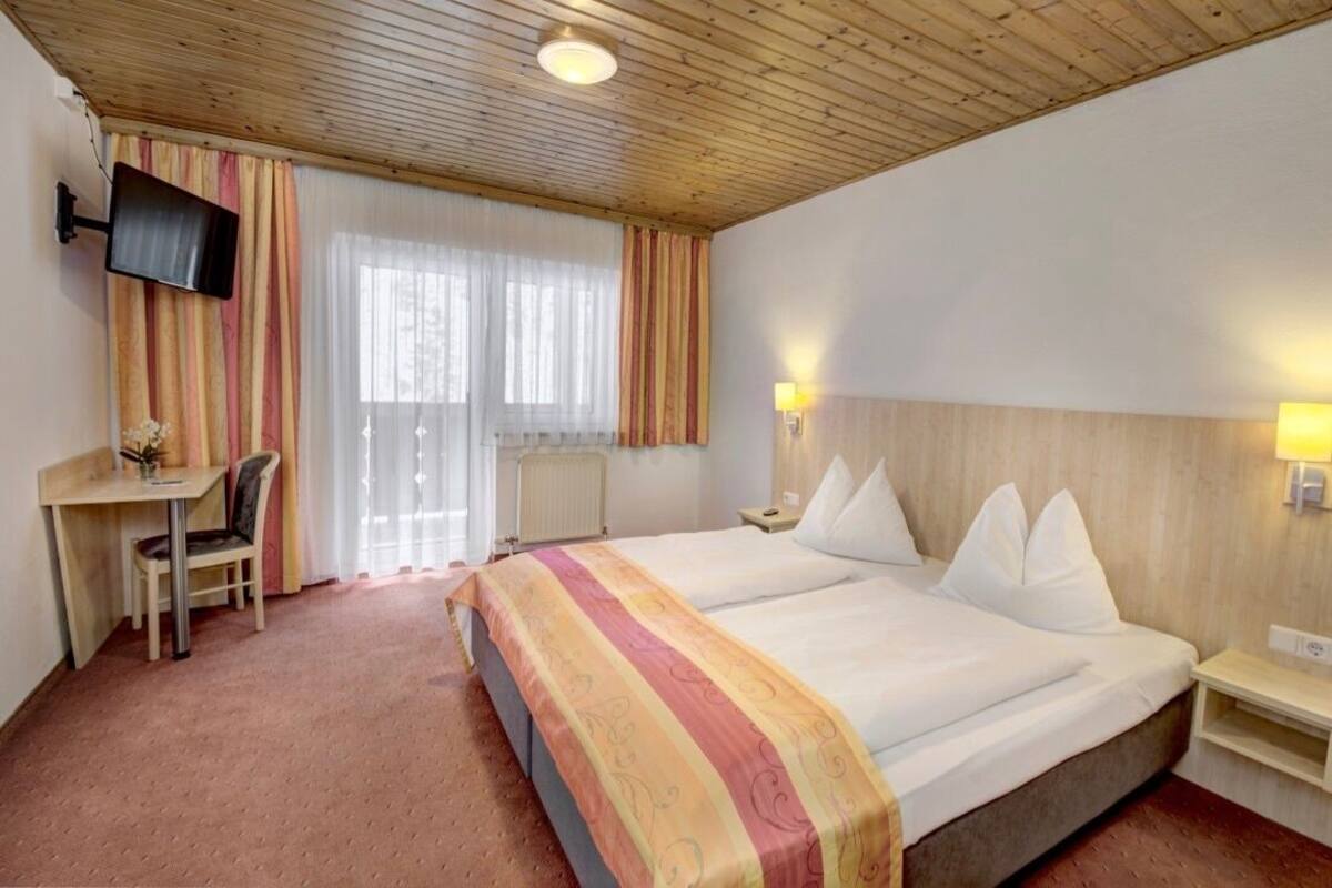Une chambre d’hôtel avec deux lits, un bureau avec une chaise, un téléviseur fixé au mur et deux lampes de chevet.