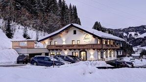A hotel with a ski lift sign, multiple cars parked in front, and a snowy mountain backdrop. - Hotel-Restaurant Bike&Snow Lederer (Muehlbach Am Hochkoenig)