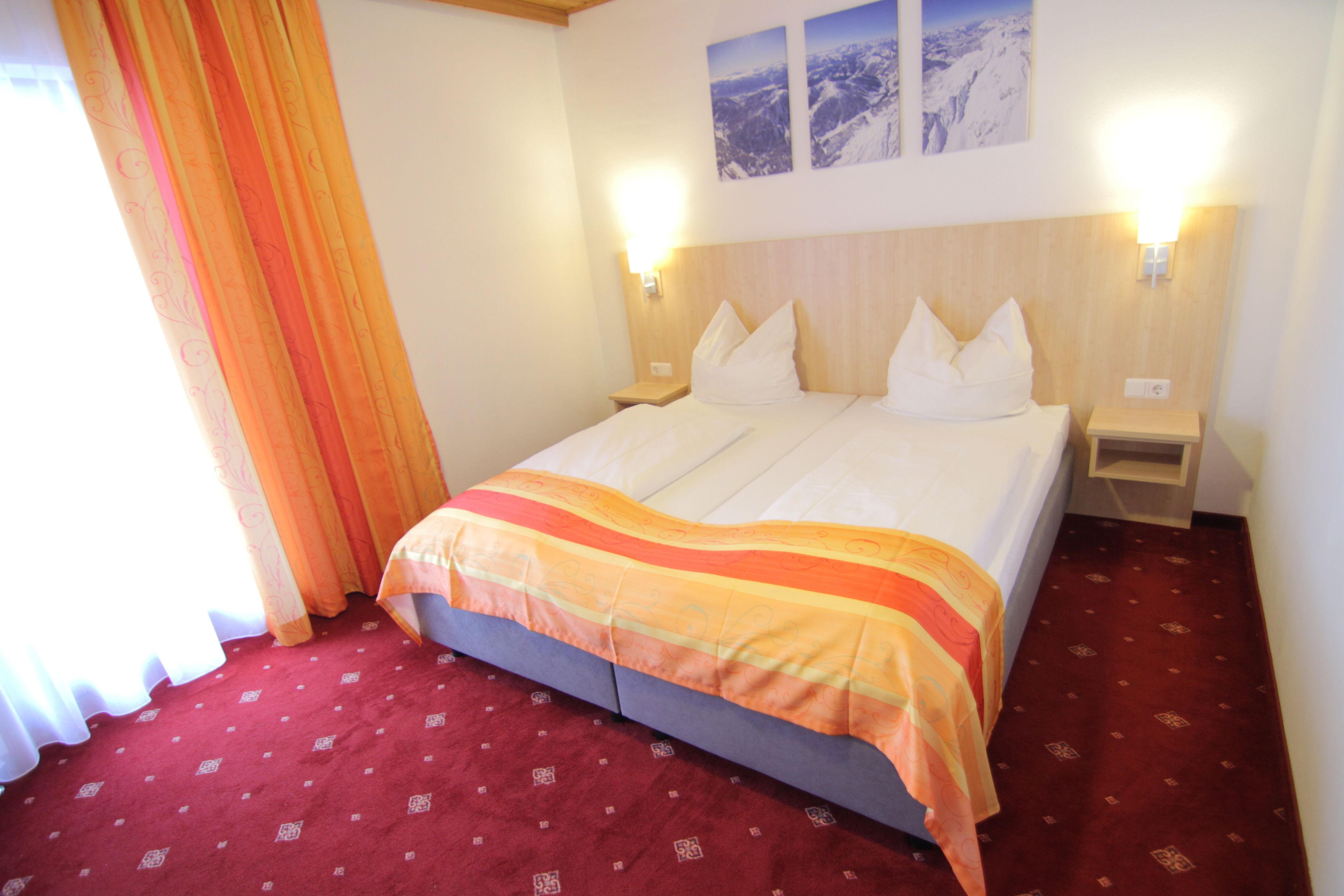 Een hotelkamer met een bed, twee nachtkastjes, een rood tapijt en twee wandlampen.