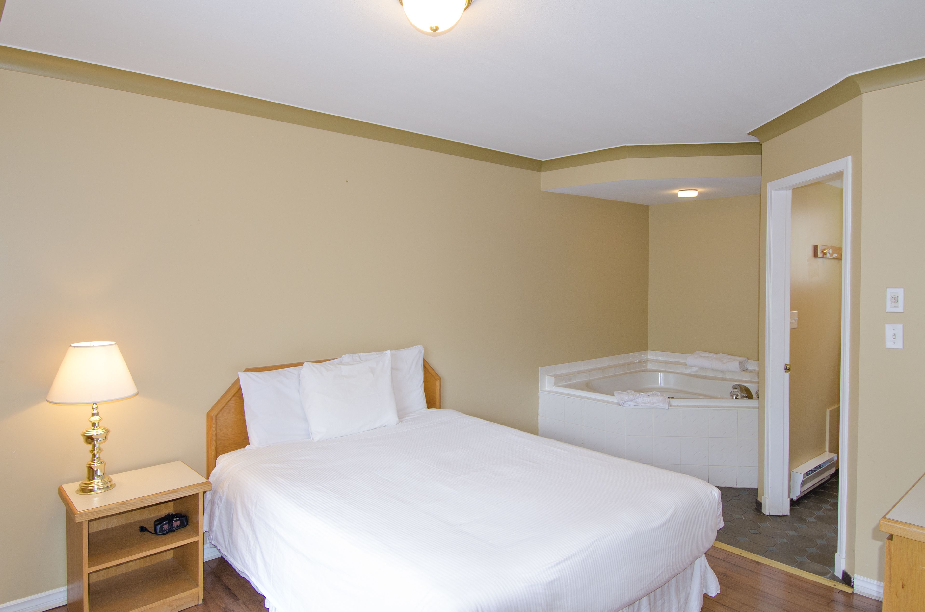 A hotel room with a bed, a nightstand with a lamp, and a separate bathroom with a bathtub.