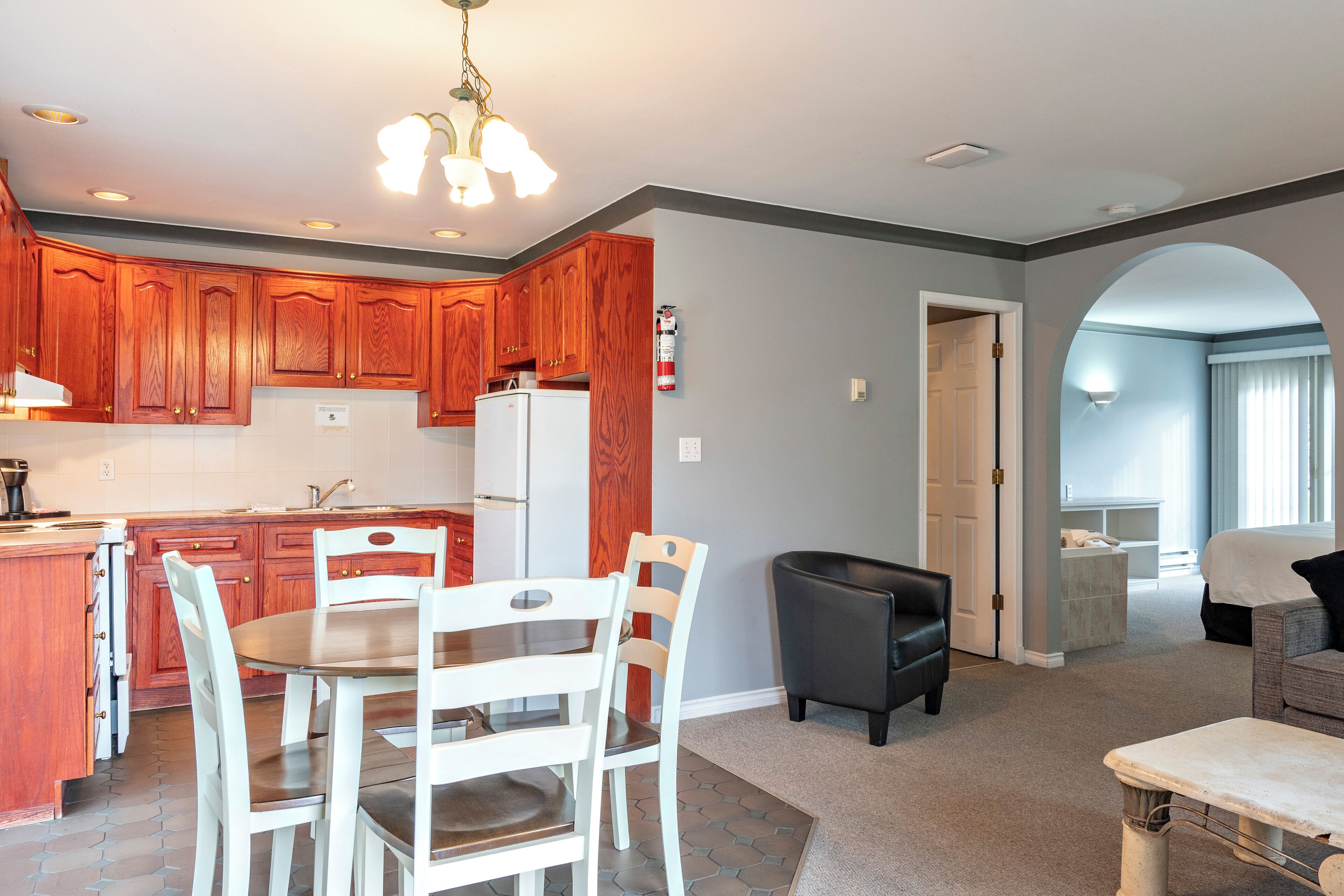 A modern kitchen with wooden cabinets, a white refrigerator, and a dining area with white chairs.