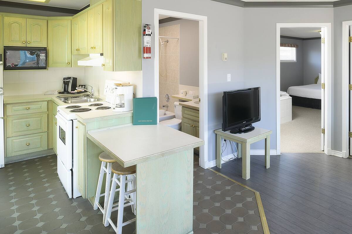 A compact hotel room with a kitchenette, a small bathroom, and a bedroom with a bed and nightstand.