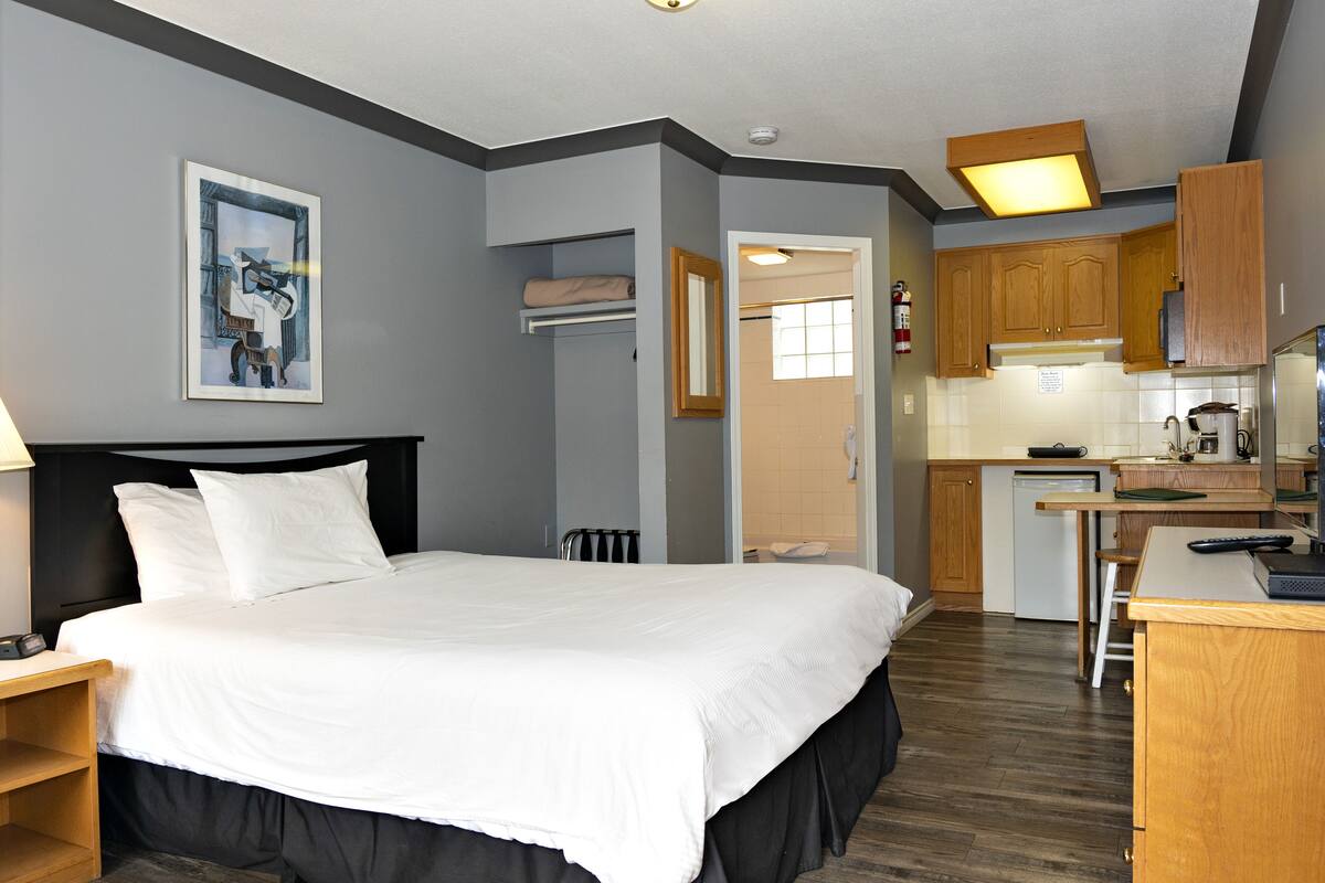 A hotel room with a bed, a desk, a kitchenette, and a bathroom.
