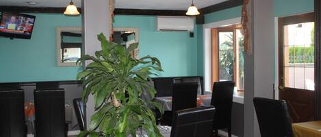 A restaurant with teal walls, black leather chairs, and a large potted plant.