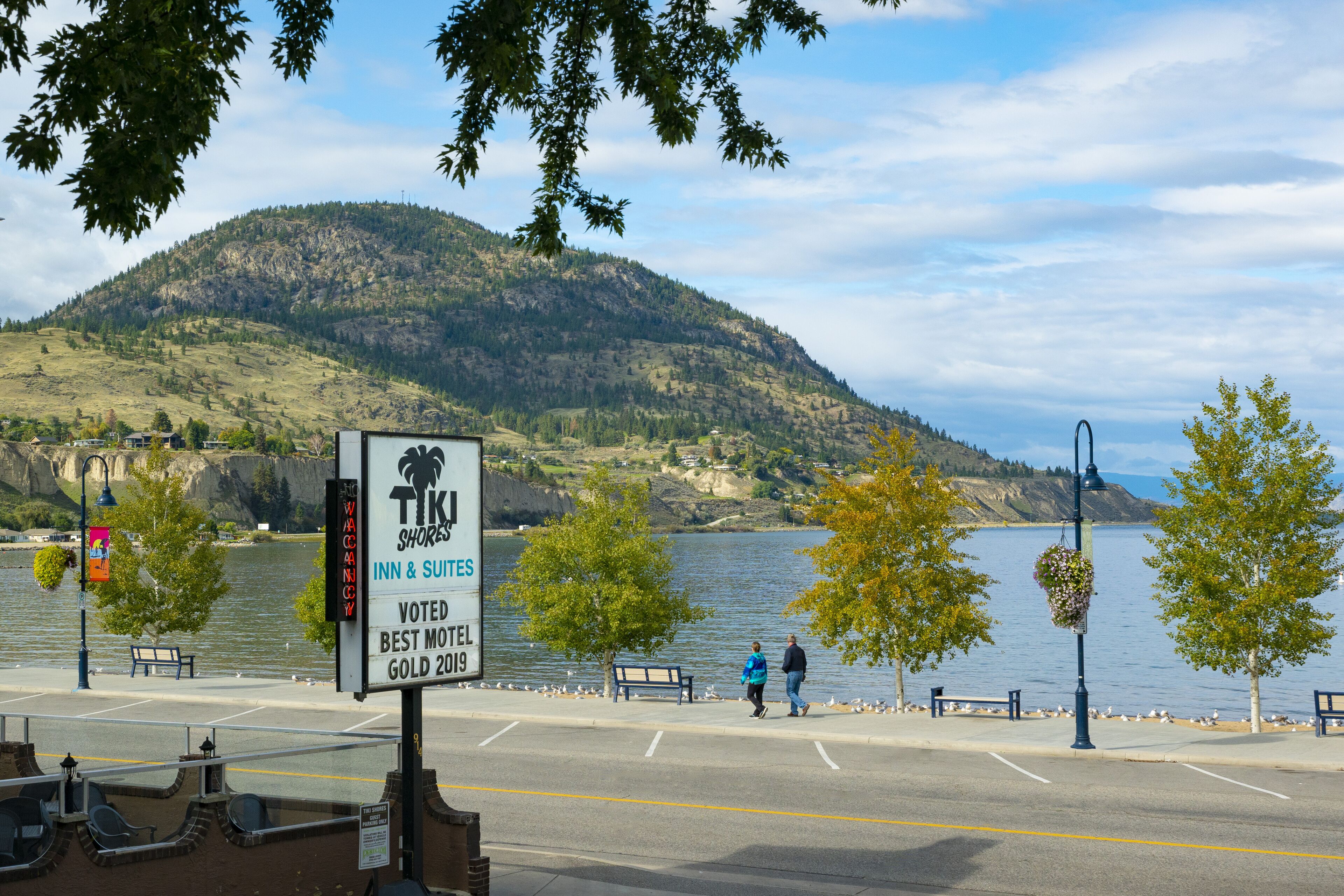 Une enseigne indiquant l’hôtel « Tik Shore Inn & Suites », avec en arrière-plan une vue sur un lac et des montagnes.