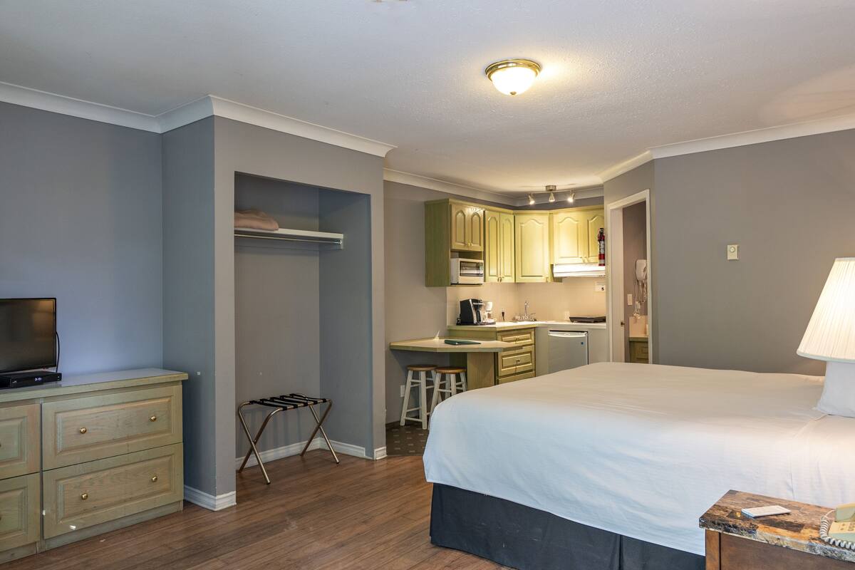A bedroom with a large bed, a desk, and a kitchenette.