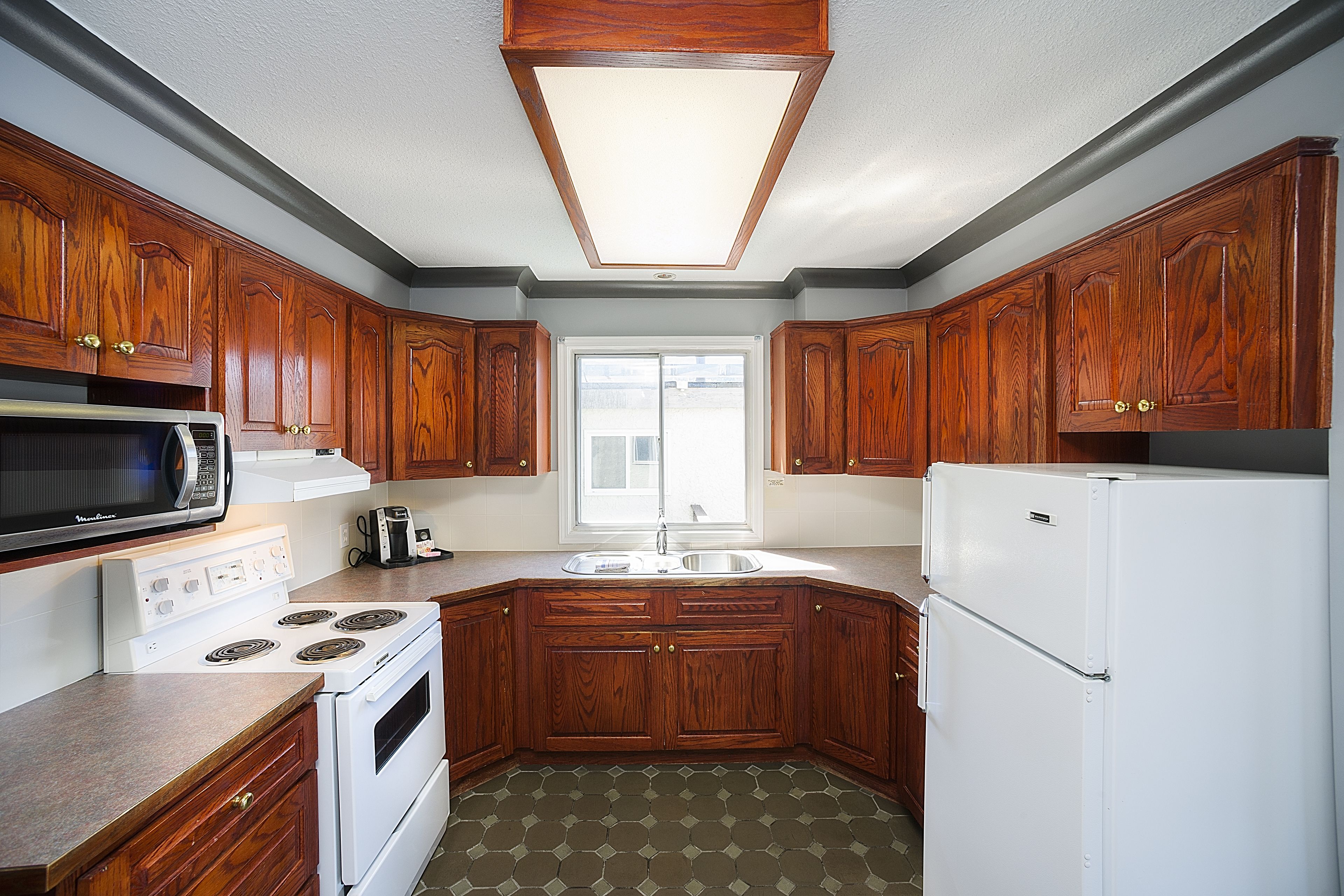 A kitchen with wooden cabinets, a microwave, stove, sink, and a refrigerator.