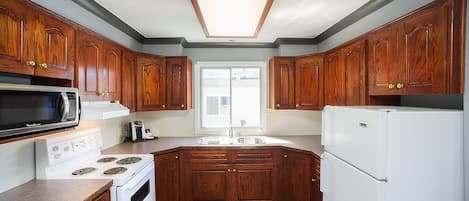 Una cocina con armarios de madera, microondas, estufa, lavaplatos y refrigerador.