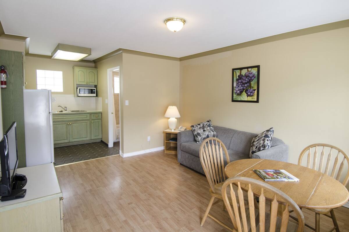 A compact living space with a kitchenette, a dining area with a table and chairs, and a sofa with a lamp.