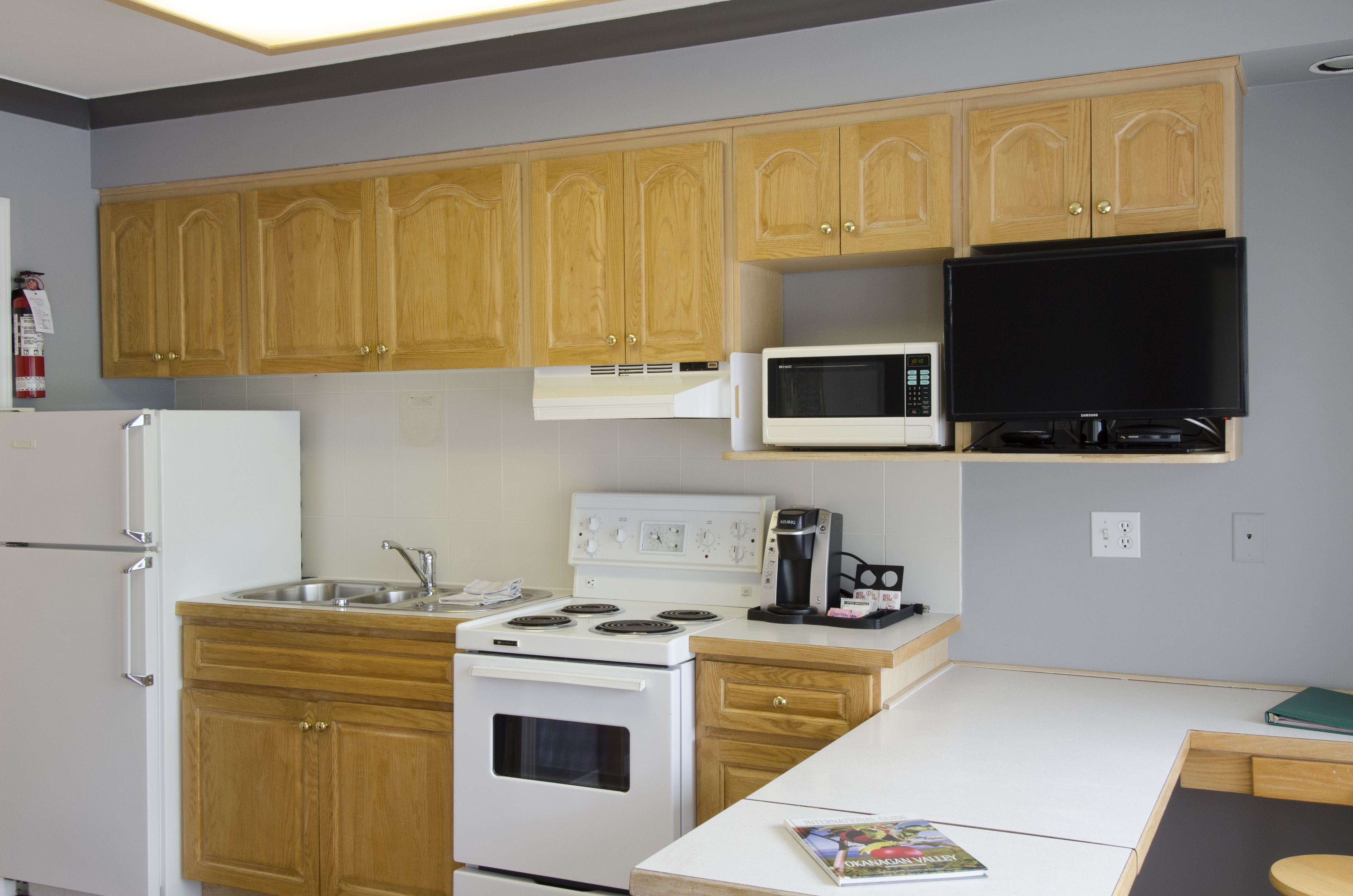 A compact kitchen with wooden cabinets, a white stove, a microwave, and a small dining area.