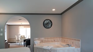 A modern bathroom with a large bathtub, a shower, and a toilet. There is a chair and a table in the adjacent room. - Tiki Shores Inn & Suites (Penticton)